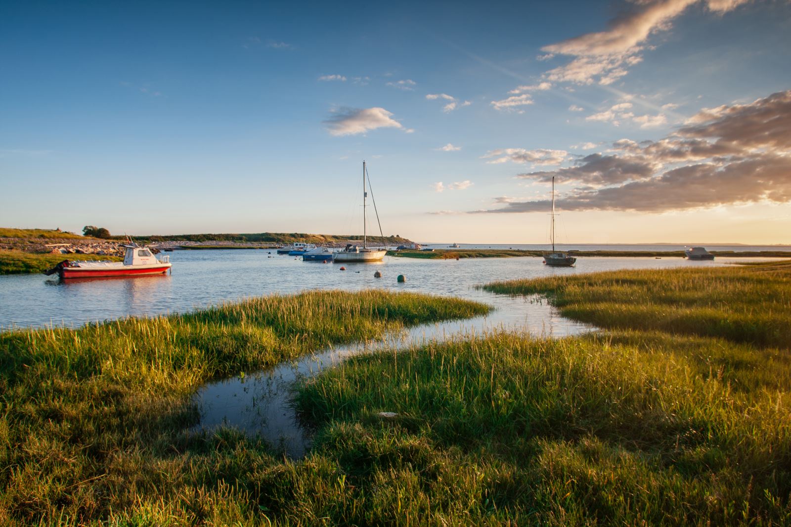 Boats moored in water beyond the green reeds of the sea marshes